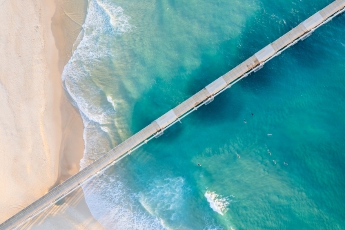 Looking directly down at a jetty with the blue ocean waves meeting the beach sand - Australian Stock Image