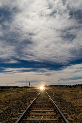 Looking down a Railway track with shining light in the distance on a starry cloudy night - Australian Stock Image