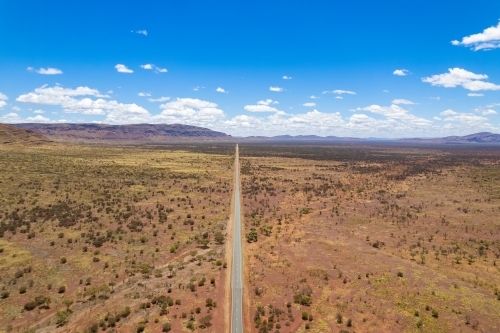 Looking down at a long straight asphalt road with the mountains in the distance - Australian Stock Image