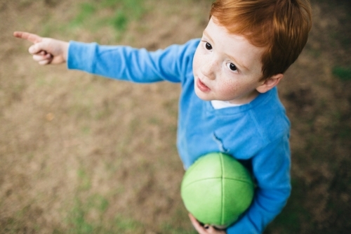 Looking down at a young boy holding a football and pointing - Australian Stock Image