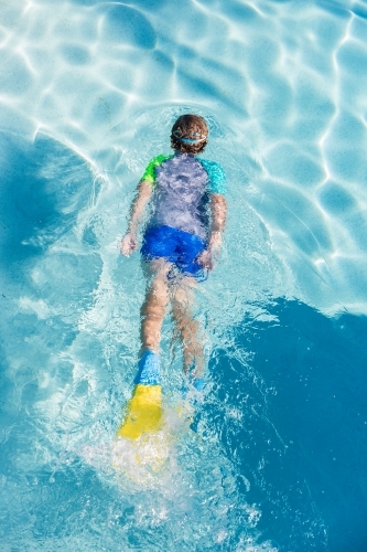 Looking down at boy wearing flippers and goggles gliding in swimming pool - Australian Stock Image