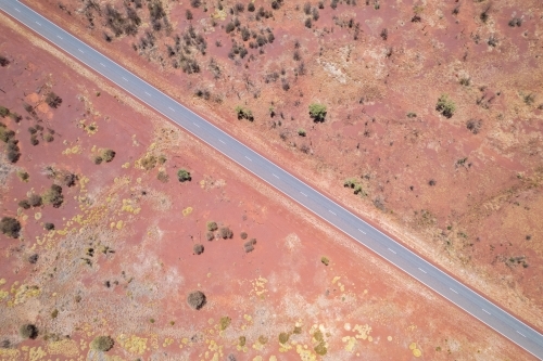 Looking down at the diagonal asphalt road with the red dirt and bushes on both sides of t - Australian Stock Image
