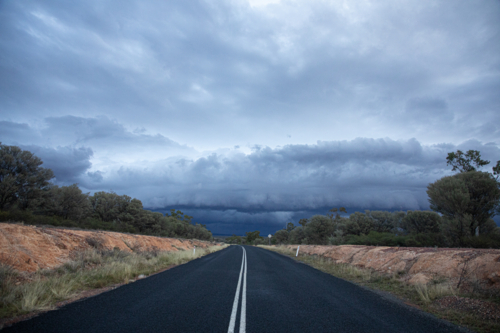 Looking down double white lines on a bitumen road towards a shelf cloud. - Australian Stock Image