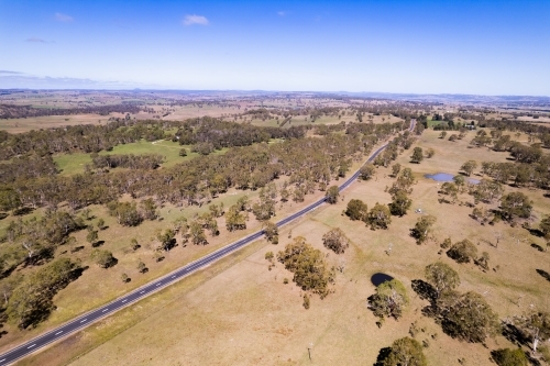 Looking down on a brown rural countryside with a single asphalt highway going off in the distance - Australian Stock Image