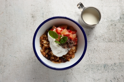Looking down on bowl of muesli, fresh fruit and yoghurt next to jug of milk - Australian Stock Image