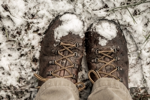 looking down on worn old leather boots in snow