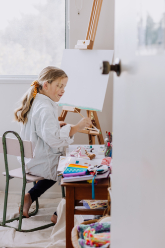 Looking into a room where Girl painting on canvas at home studio - Australian Stock Image