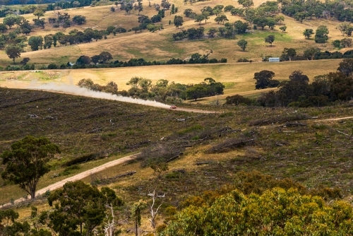 Looking on a distant rally car speeding along a country road with dust trailing behind - Australian Stock Image