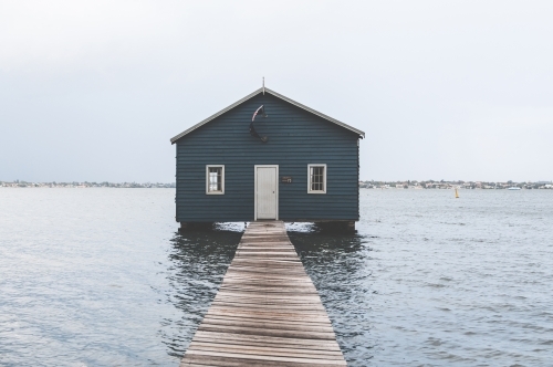 Looking out along a pier to a blue boat shed on a river