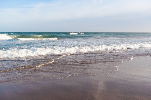 Looking out from beach at waves breaking in the ocean as the tide comes in. - Australian Stock Image