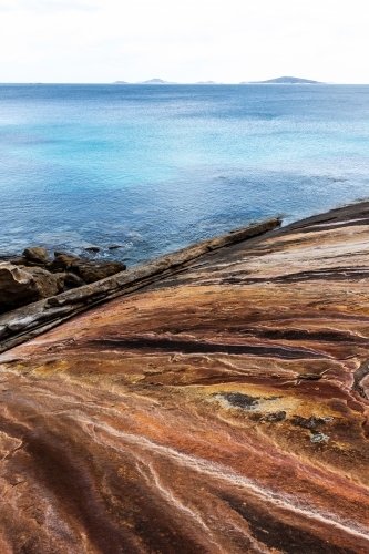 Looking out over patterned, textured, colourful rock face toward the ocean - Australian Stock Image