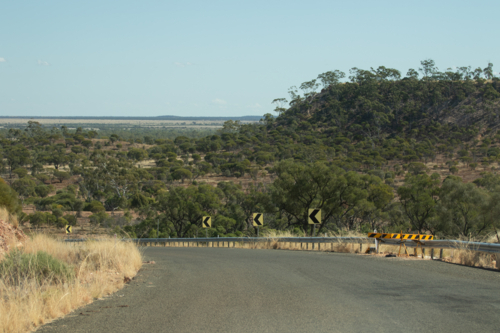 Looking over a bend in the bitumen road to the outback landscape beyond - Australian Stock Image