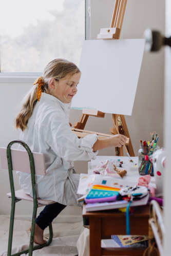 Looking through a door into a home studio where girl is painting on canvas - Australian Stock Image