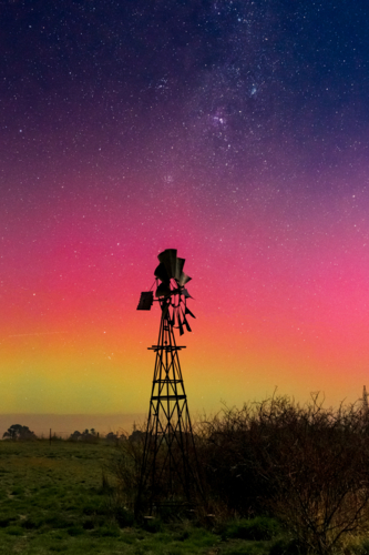 Looking up at a starry night above colourful Aurora Australis over a silhouetted windmill - Australian Stock Image