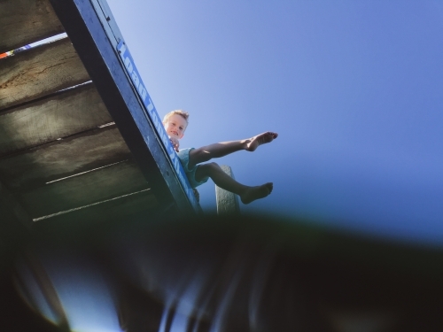 Looking up from the water at boy sitting on jetty - Australian Stock Image