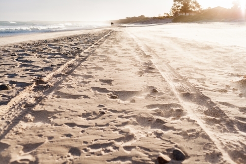 Loose sand blows through the air over detailed tyre tracks of a 4wd on the beach at sunset - Australian Stock Image