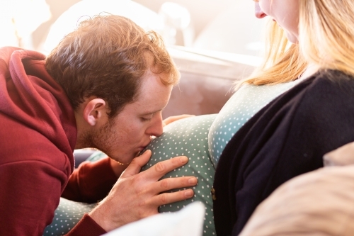 Loving husband kissing belly of pregnant wife - Australian Stock Image