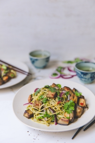 Low angle of cold soba noodle, eggplant and parsley salad with green tea on white background