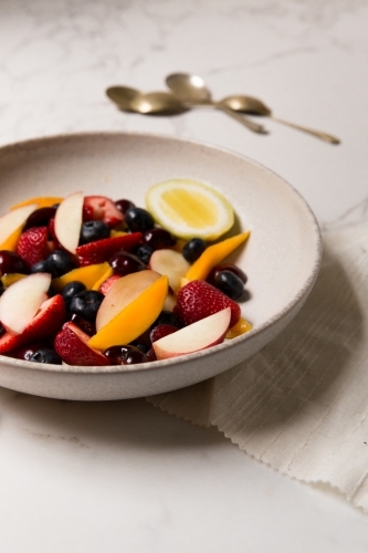 Low angle of styled, naturally lit and colourful mixed berry and stone fruit salad on marble table