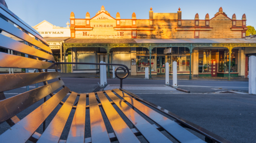Low angle view of a street bench reflecting an historic building facade bathed in golden light - Australian Stock Image