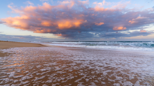 Low angled view of a colourful storm clouds over waves breaking in a sandy beach at twilight - Australian Stock Image