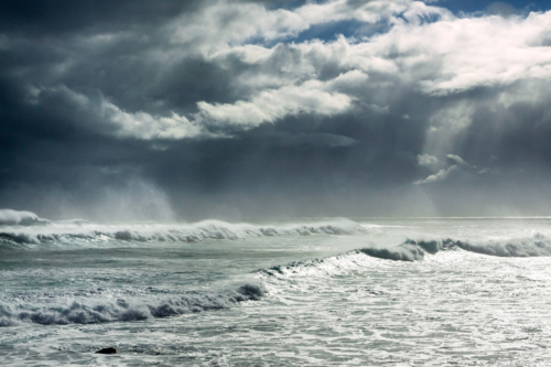 Low angled view of a dark stormy sky over large breaking waves - Australian Stock Image