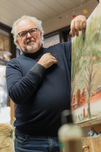 Low angled view of a distinguished male artist leaning on a painting in an art studio