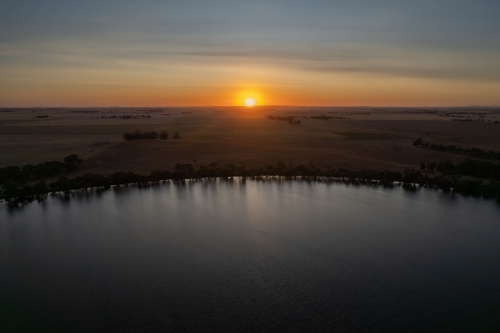 Low sun over landscape with lake in foreground - Australian Stock Image