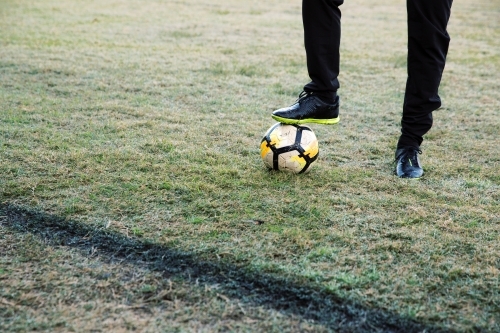 Lower body extremity shot of a man standing on the field stepping on a soccer ball with one foot - Australian Stock Image