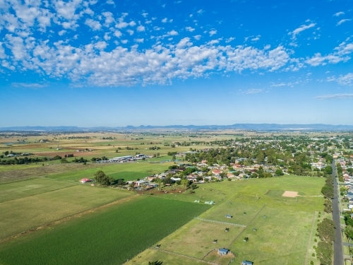 lush green farm paddocks and edge of country town on bright sunlit day - Australian Stock Image