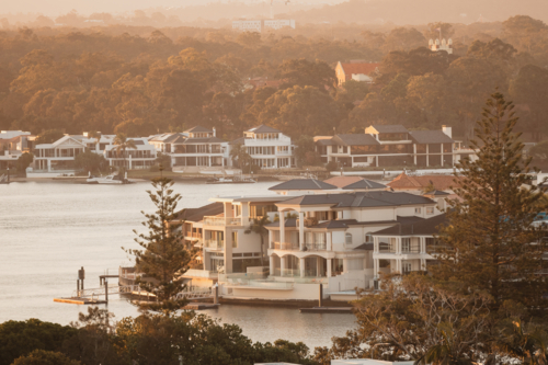 Luxury waterfront mansions line a serene river at golden hour - Australian Stock Image