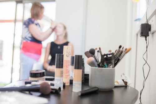 Makeup products with woman getting makeup done in background - Australian Stock Image