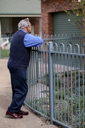 Male Aboriginal elder leaning against a fence turned away from the camera