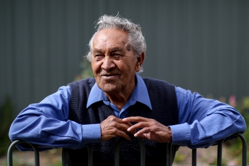 Male Aboriginal elder smiling and leaning against fence