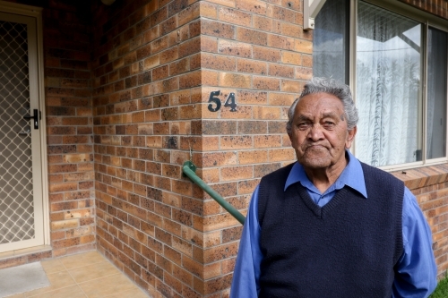 Male Aboriginal elder standing in front of his home