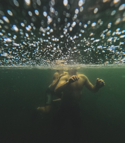 Male adult with child on back underwater with bubbles on water surface - Australian Stock Image