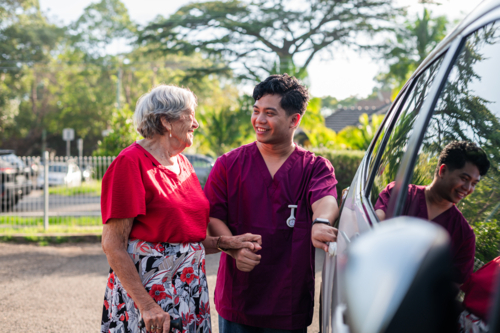 Male caregiver helping an elderly woman get into the vehicle - Australian Stock Image