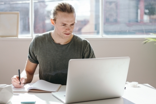Male designer looking at a laptop screen in a bright white studio - Australian Stock Image
