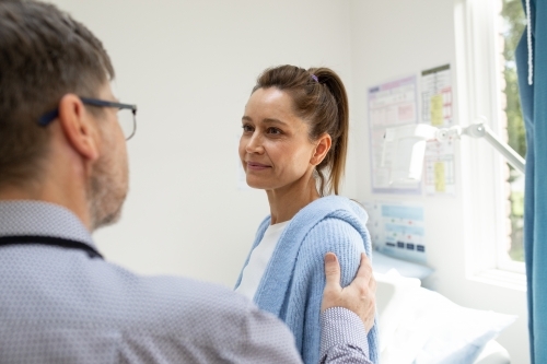 Male doctor placing his hand on his female patient's shoulder, reassuring her