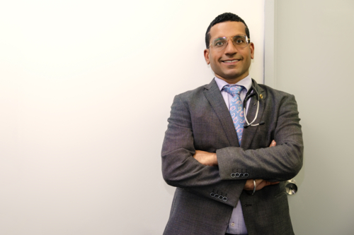 Male doctor standing with arms crossed against white wall - Australian Stock Image