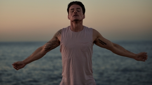 Male doing stretch exercise beside ocean - Australian Stock Image