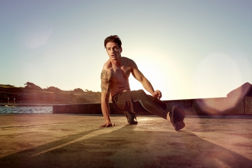 Male doing stretch exercise beside ocean - Australian Stock Image