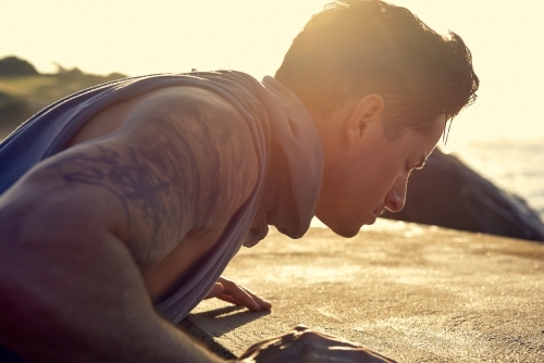 Male doing stretch exercise beside ocean - Australian Stock Image