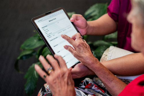 Male healthcare worker holding tablet device for an elderly woman tapping on the screen - Australian Stock Image