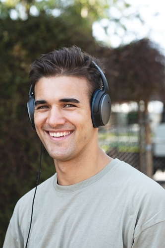 Male in his twenties wearing headphones and listening to music outdoors in the local park