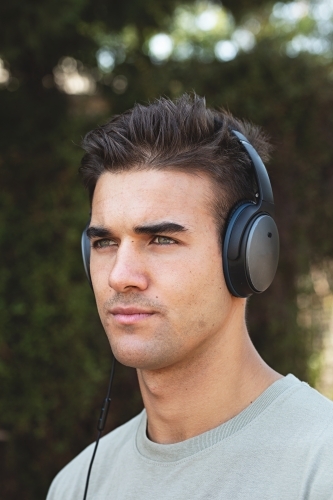 Male in his twenties wearing headphones and listening to music outdoors in the local park - Australian Stock Image