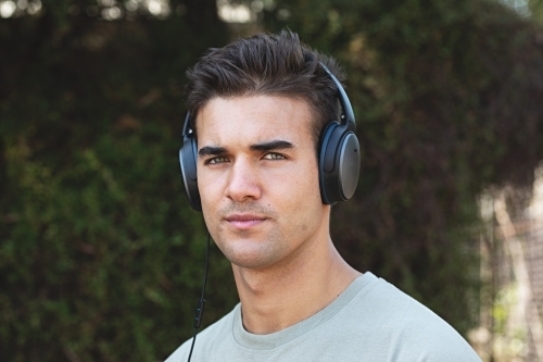 Male in his twenties wearing headphones and listening to music outdoors in the local park