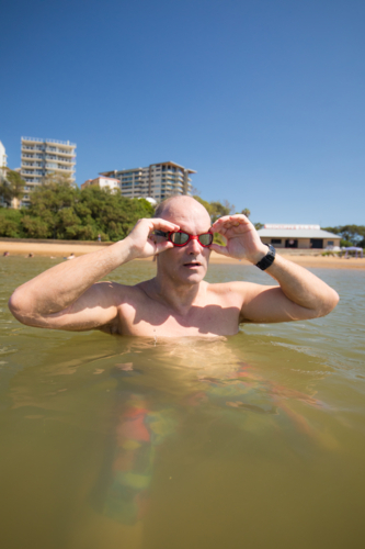 Male middle aged swimmer adjusting goggles while standing in the water - Australian Stock Image