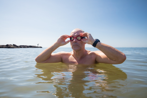 Male open water swimmer adjusting goggles while standing in water - Australian Stock Image