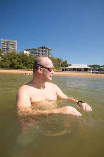 Male open water swimmer wearing goggle standing in water near the shore - Australian Stock Image